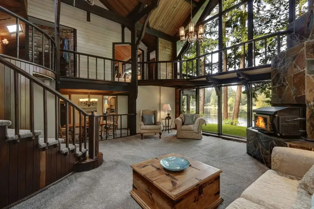 Modern wooden cottage house interior with living room close up. Gorgeous fireplace with natural stone tile trim and large glass wall. Northwest, USA