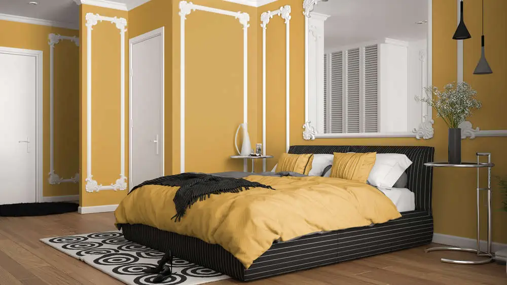 Modern yellow colored bedroom in classic room with wall moldings, parquet, double bed with duvet and pillows, minimalist bedside tables, mirror and decors. Interior design concept
