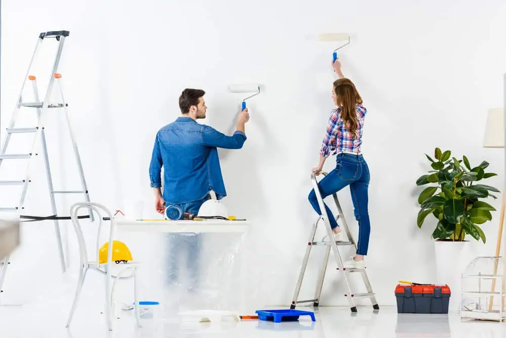 rear view of couple painting wall with white paint