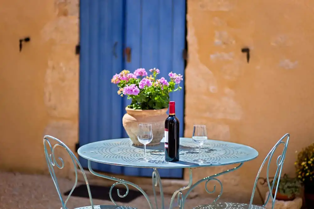 Table for two set with red wine in front of a rustic country house. The wall is painted in ochre with wooden door in blue.