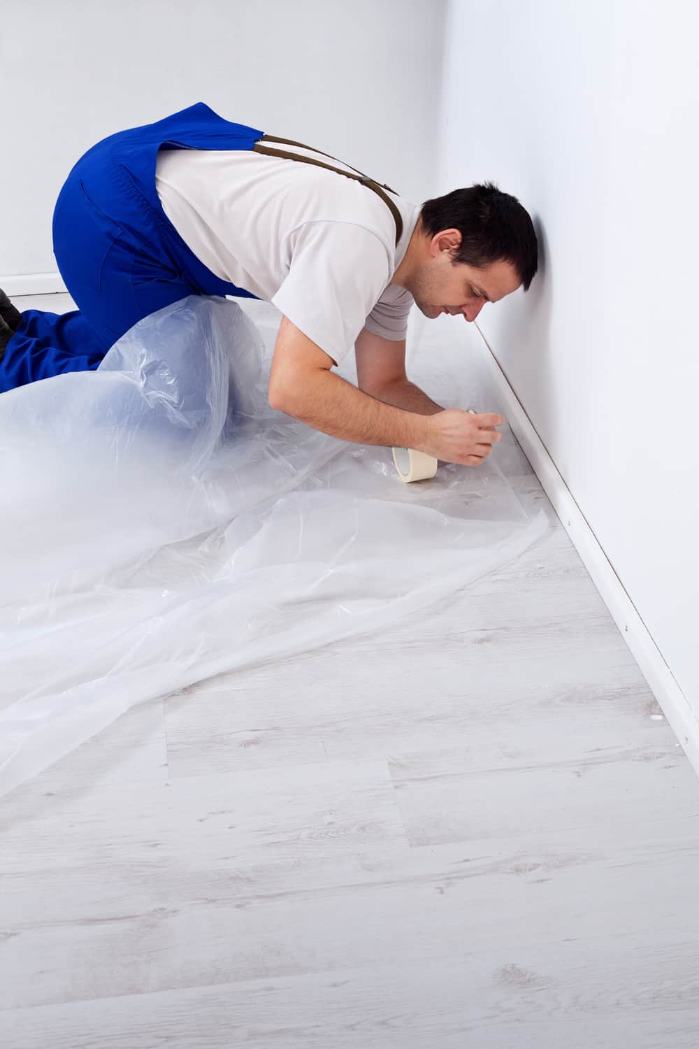 Worker laying protection film before painting - kneeling on the floor