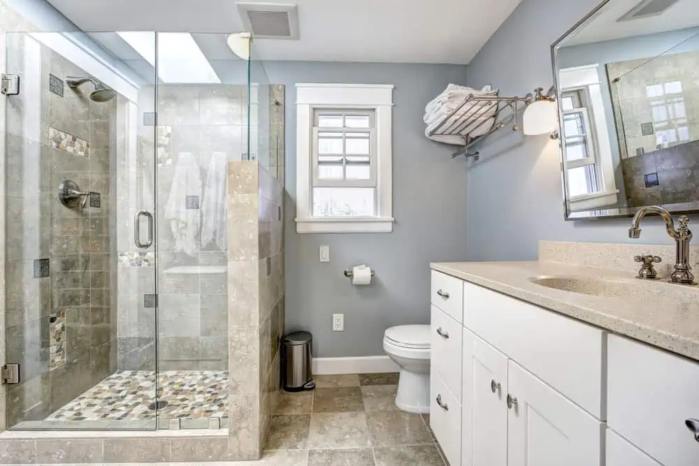 Light blue modern bathroom interior with glass door shower and white cabinet with mirror