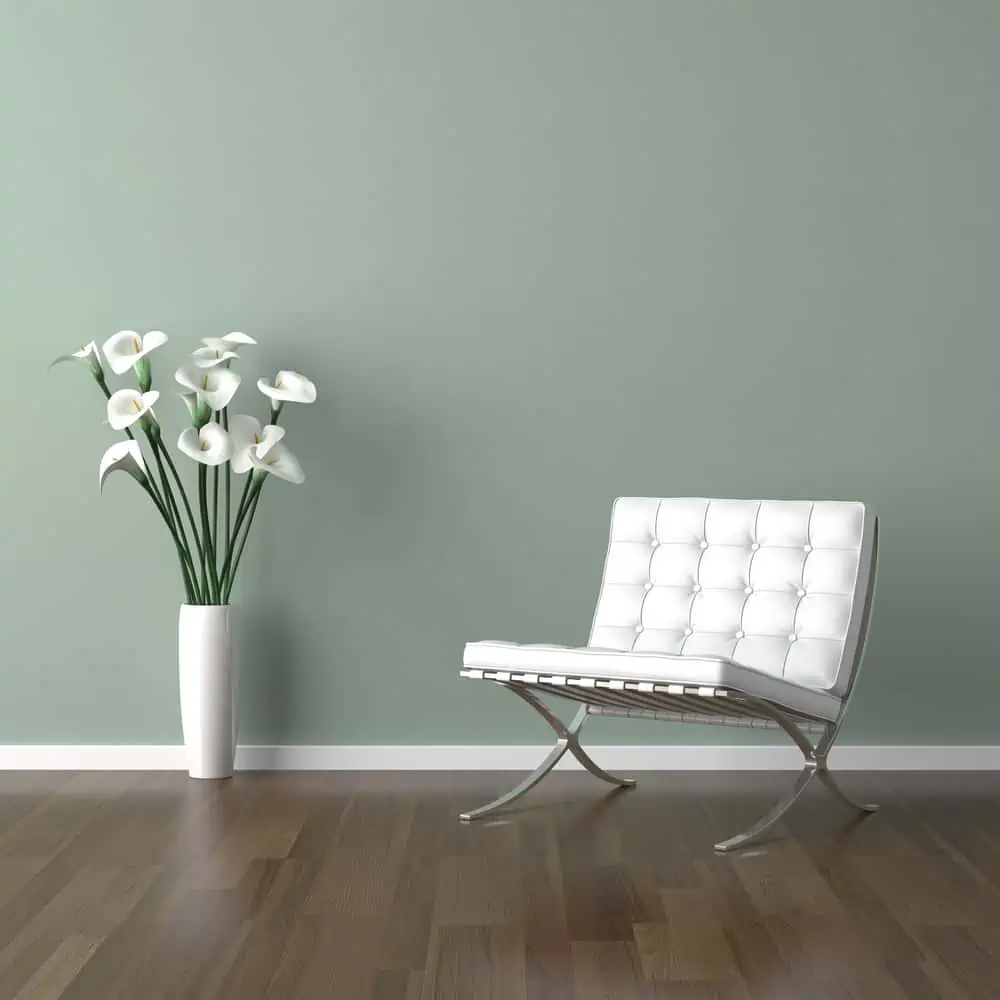 interior design scene with a white modern chair and avase of calla lillys on a pale green wall