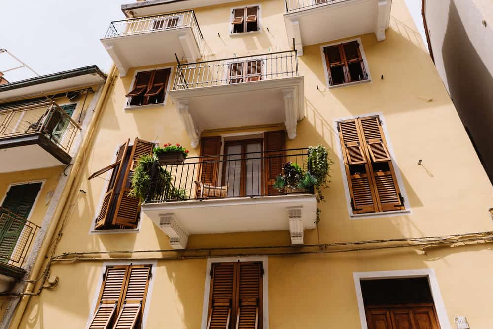 Large yellow Italian house with colourful Windows and vases. Stylish home. Open balconies and wooden window shutters