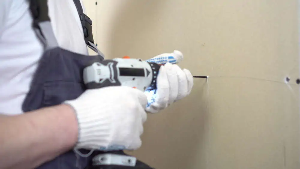 The builder screws the gypsum board with a self-tapping screw using a screwdriver on the wall closeup. 4k