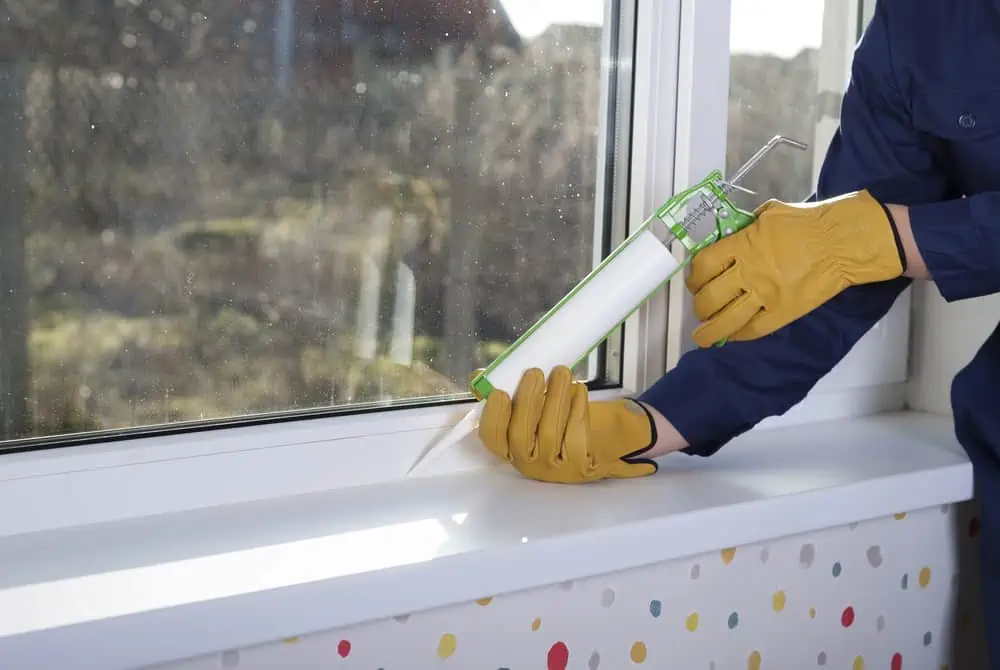 construction worker caulking window frame with silicone sealant