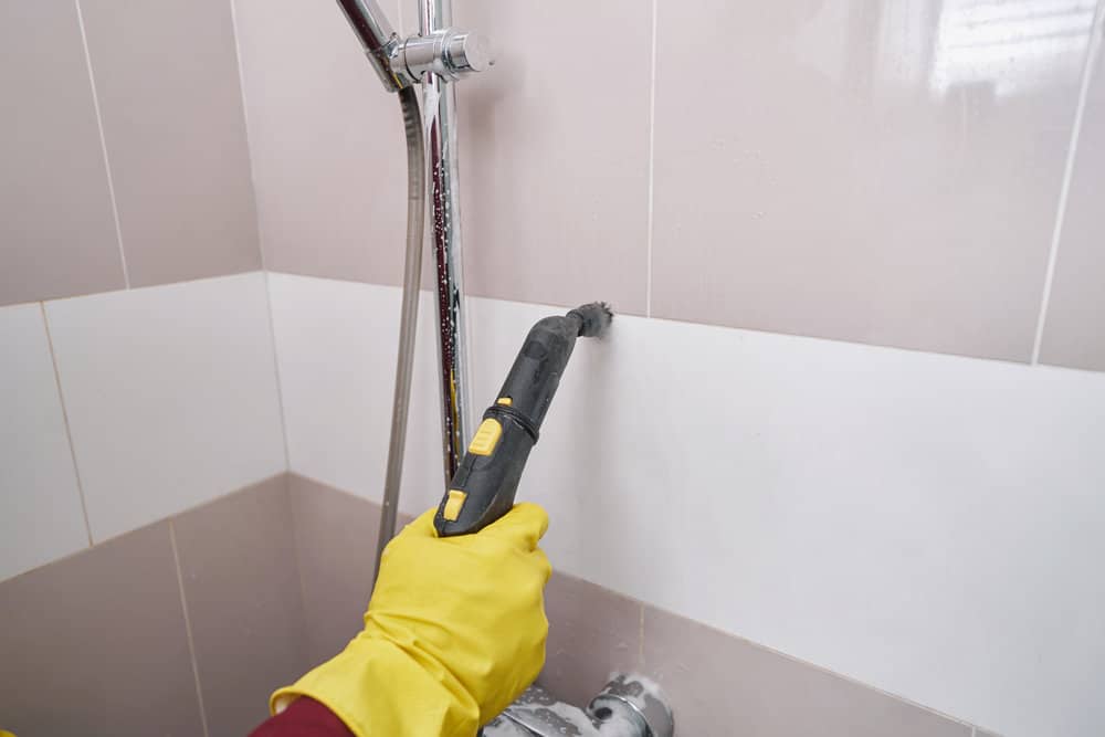Professional housecleaner steam-cleaning grout line on wall
