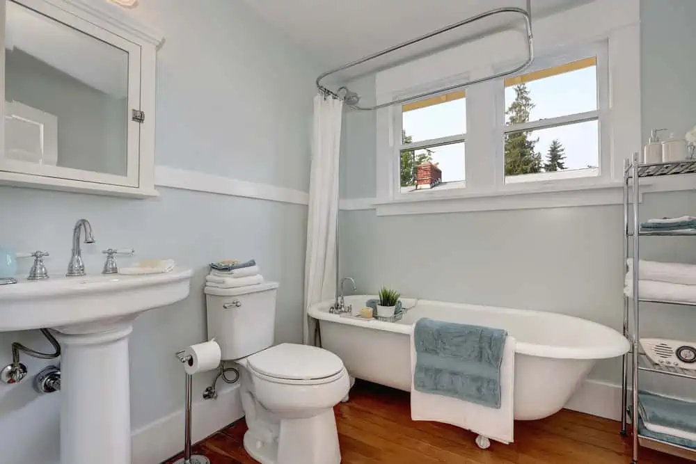 Interior design of craftsman bathroom with a pedestal sink, a freestanding tub, a toilet, white tile, pastel blue walls and hardwood floors. Northwest, USA