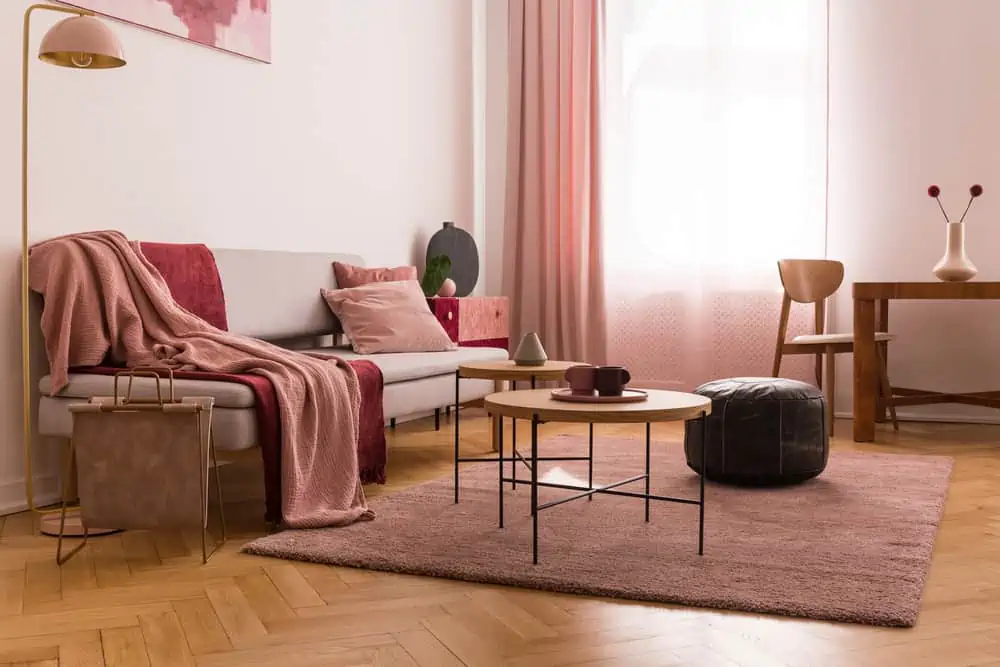 Elegant living room interior with trendy grey sofa with pastel pink pillow and burgundy blanket, wooden coffee tables next to it