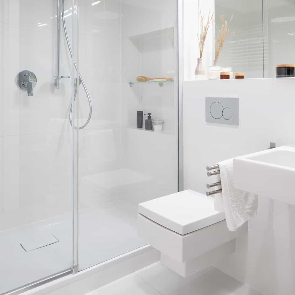 Simple and small bathroom in white with shower cabin behind glass sliding doors