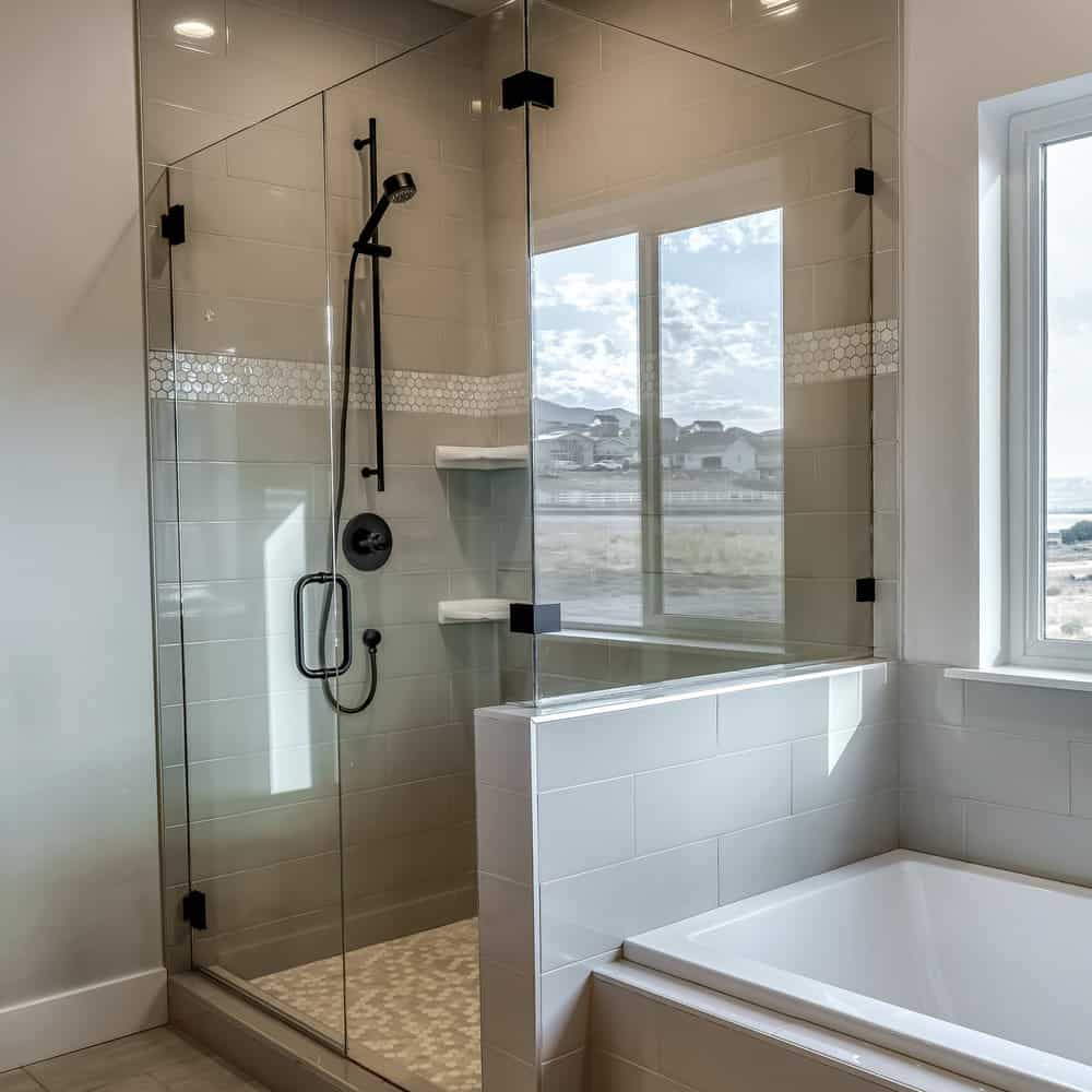 Square Rectangular walk in shower stall with half glass enclosure and black shower head. A built in bathtub is adjacent to shower stall with hinged door.