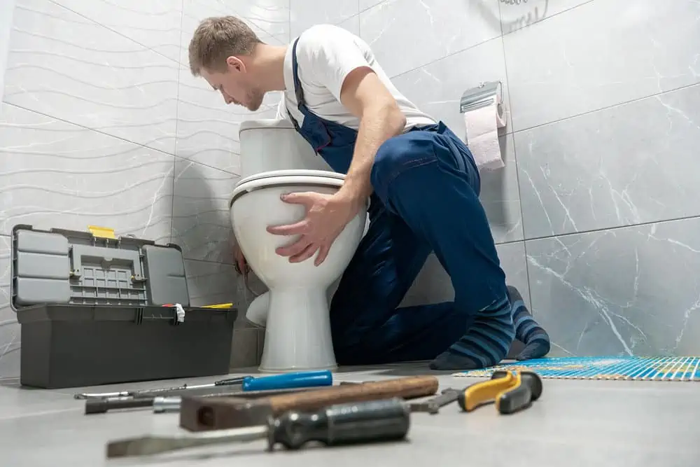 man plumber in uniform installing toilet bowl using instrument kit professional repair service.