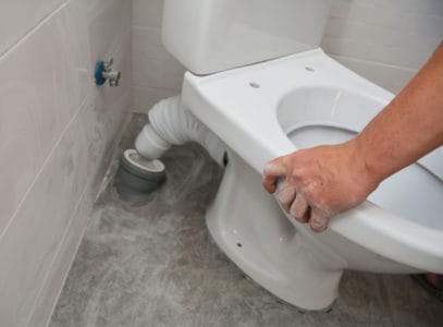 A white toilet bowl, seat installation and plumbing connecting toilet pan connector to the waste pipe and water supply pipe to the toilet tank in the corner of the bathroom.