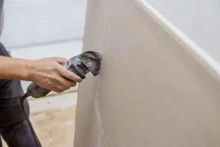 Man cutting gypsum drywall on using angle hand electric power tools
