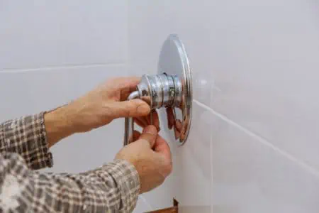 Plumber hands fixing shower mixer on modern water tap.