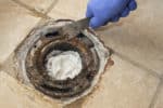 Closeup of man’s hand scraping cast iron toilet flange with caulked lead joint