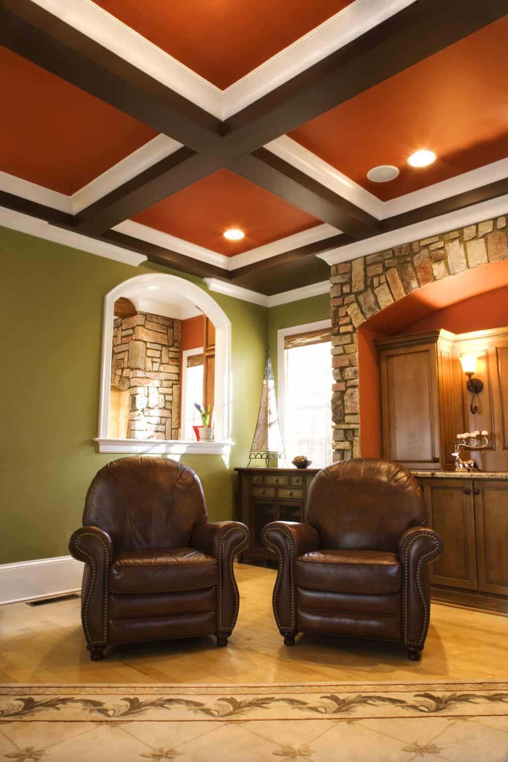 Two brown leather chairs in an upscale living room with wooden box beam ceiling and stone arch accents. Vertical shot.