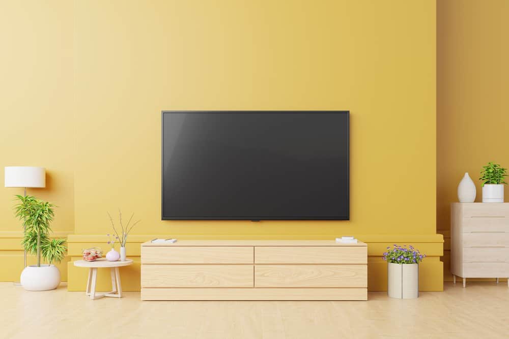 Smart Tv Mockup in modern living room with lamp,table,flower and plant on yellow wall background,3d rendering