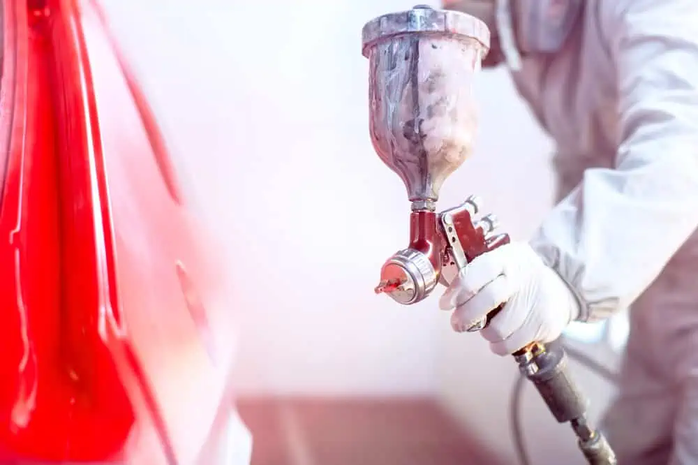 Close-up of spray gun with red paint painting a car in special b