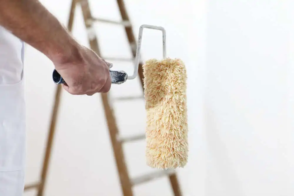 Painter at work holding paint roller with ladder in the background