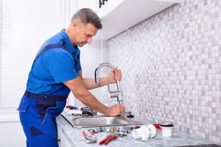 Male plumber fixing faucet in the kitchen