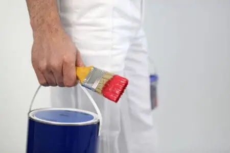 Man holding a gallon of paint and paint brush