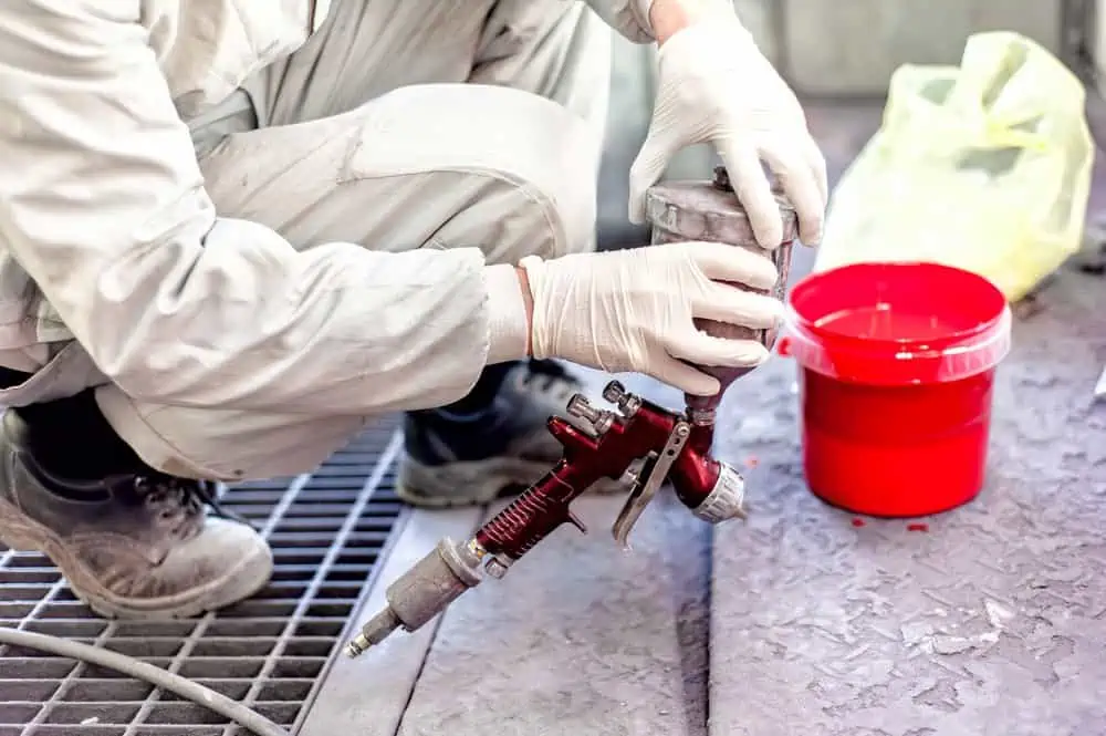 Worker holding spray gun and mixing red paint