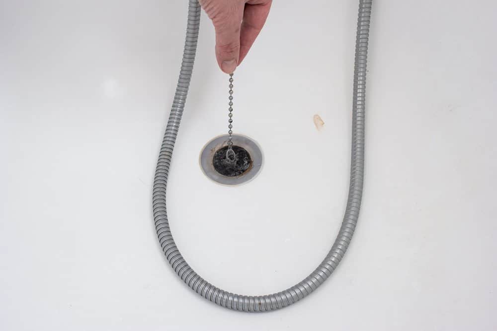 Male hand holding bathtub drain plug with chain next to shower cord