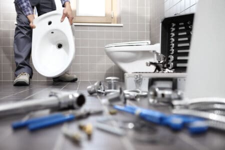 Plumber holding toilet part in the bathroom with tools on the floor
