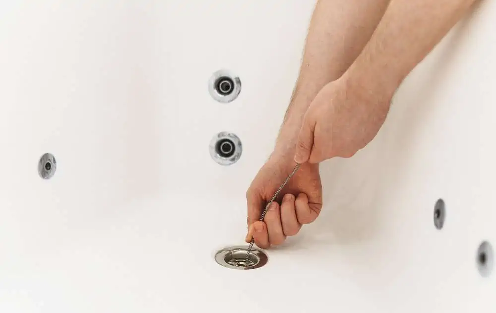 Plumber's hand using drain snake to unclog bathtub