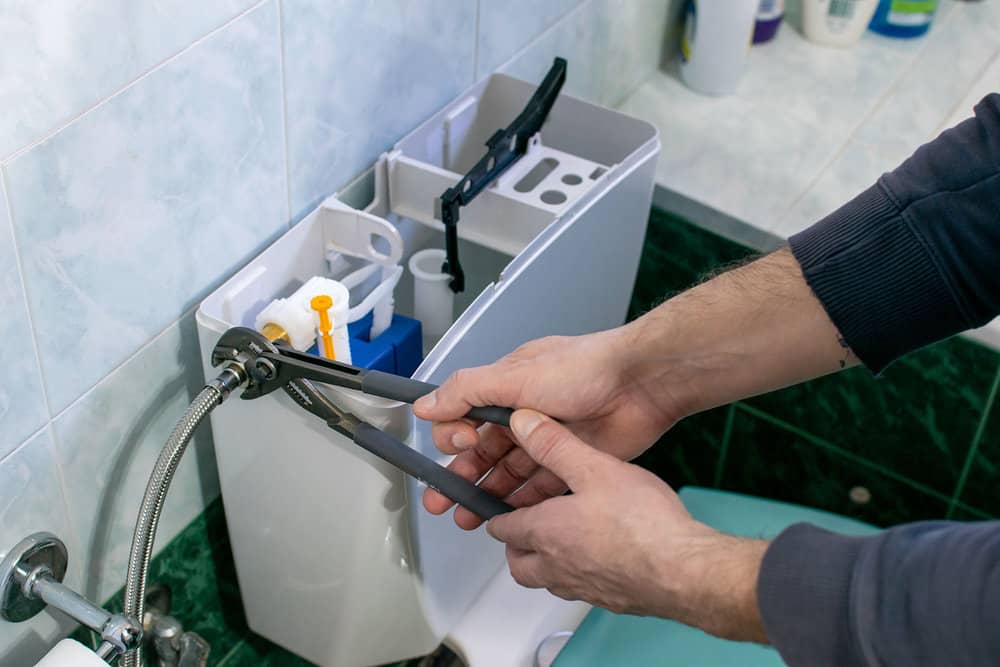 Close-up photo of man's hand turning off water to toilet using pliers