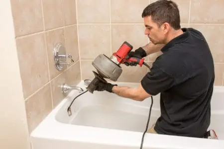 Plumber unclogging a tub drain with an electric auger