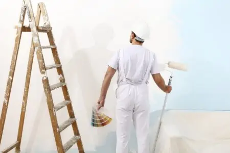 Man holding paint roller and color samples looking at the wall with stairs