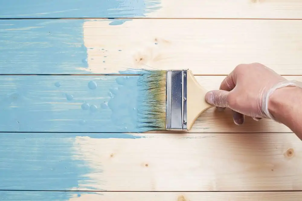 Hand holding brush with light blue paint on wood