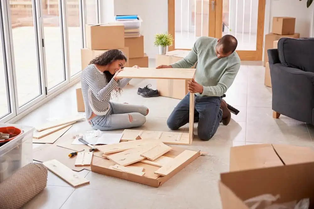 Couple sitting on the floor putting together self assembly shelf in their new home
