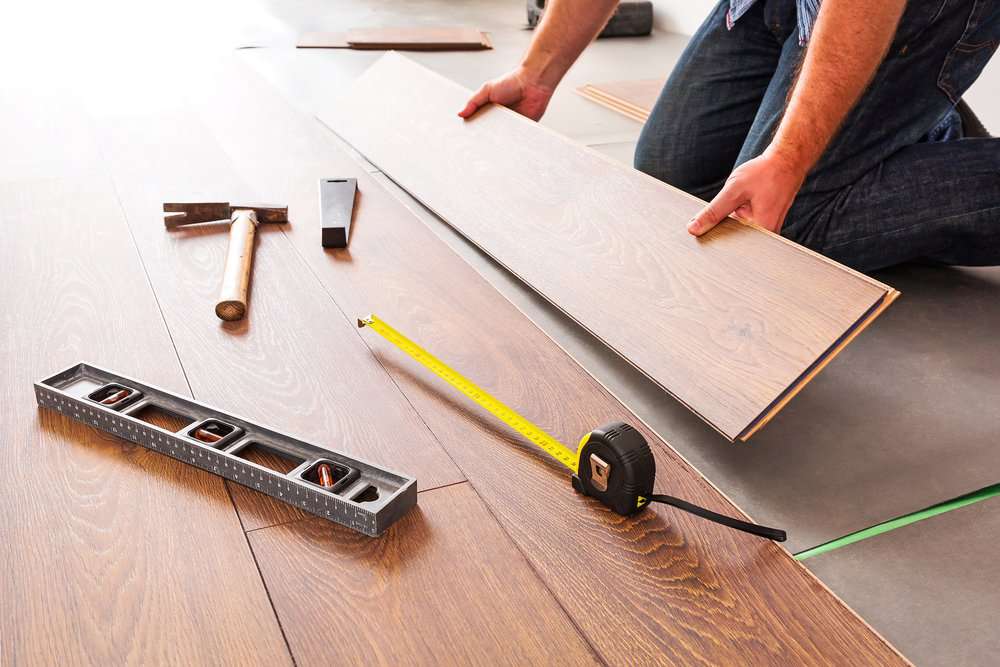 Man installing wooden flooring with various tools on the floor