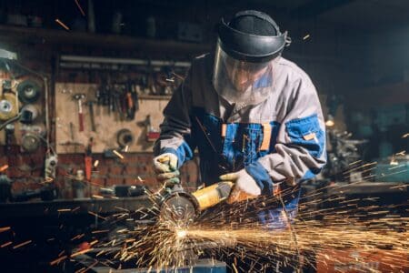 Welder in special clothes and goggles works in production with sparks