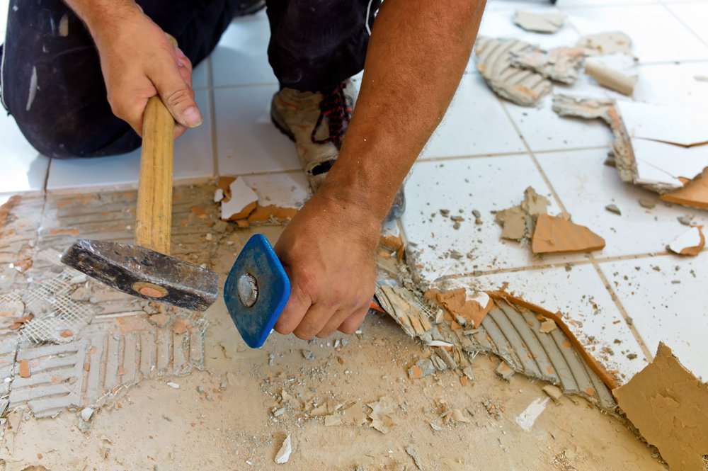 Man scraping off tiles from bathroom floor using hammer