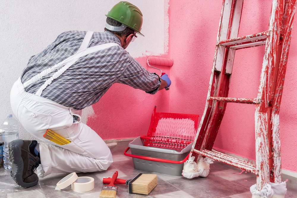 Professional house painter at work painting the wall with pink paint