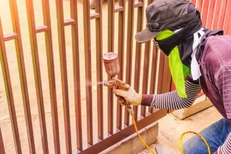 Male workers using paint sprayer at steel door