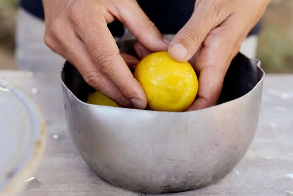Male hands washing lemon in bowl with water